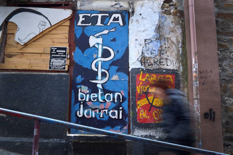 A woman walks past a mural depicting the serpent and axe emblem of armed Basque separatists ETA in Bermeo