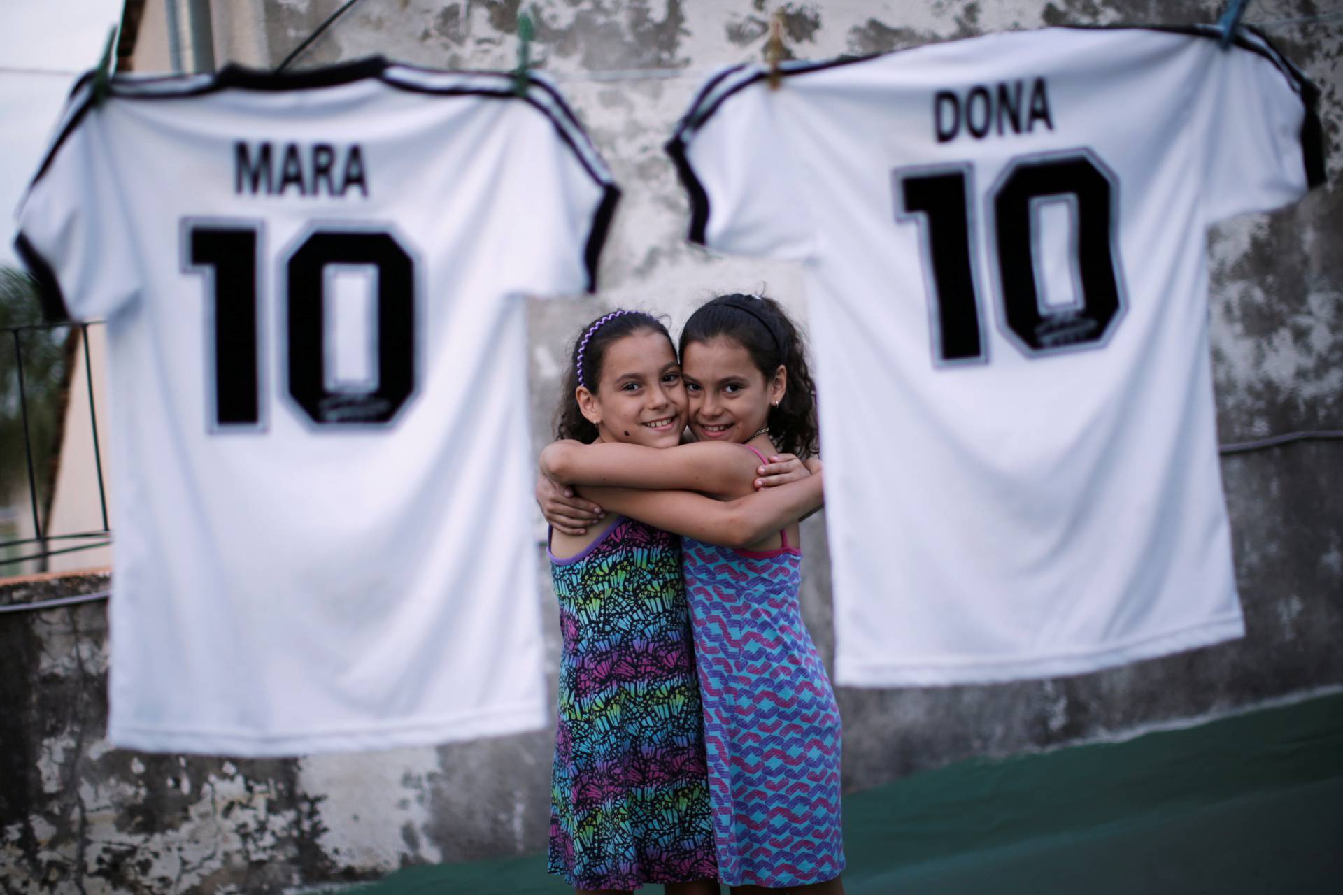 Mara and Dona, twin daughters of Walter Gaston Rotundo,a devoted Diego Maradona fan who named his daughters after the soccer star, pose near t-shirts with their names, in Buenos Aires
