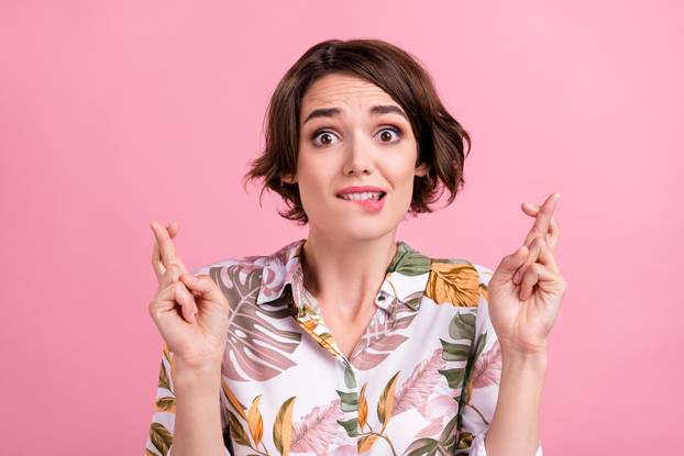 Photo of young girl bite lips teeth crossed fingers worried hope luck success isolated over pink color background