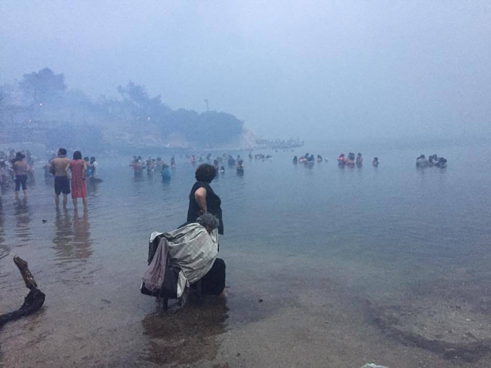 People are seen as a wildfire burns in Mati