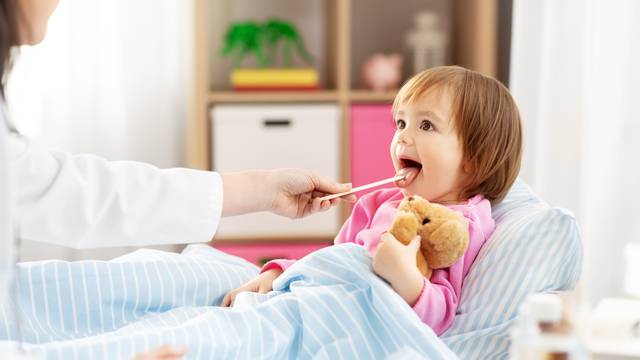doctor checking sick girl's throat at home