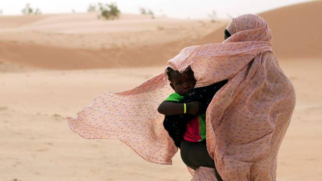 FILE PHOTO: A woman shields her child from the wind while walking on sand dunes in Nouakchott