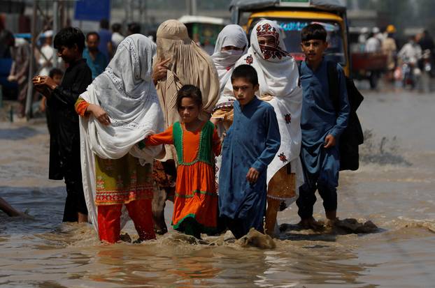 A family walk along a flooded street, following rains and floods during the monsoon season in Nowshera