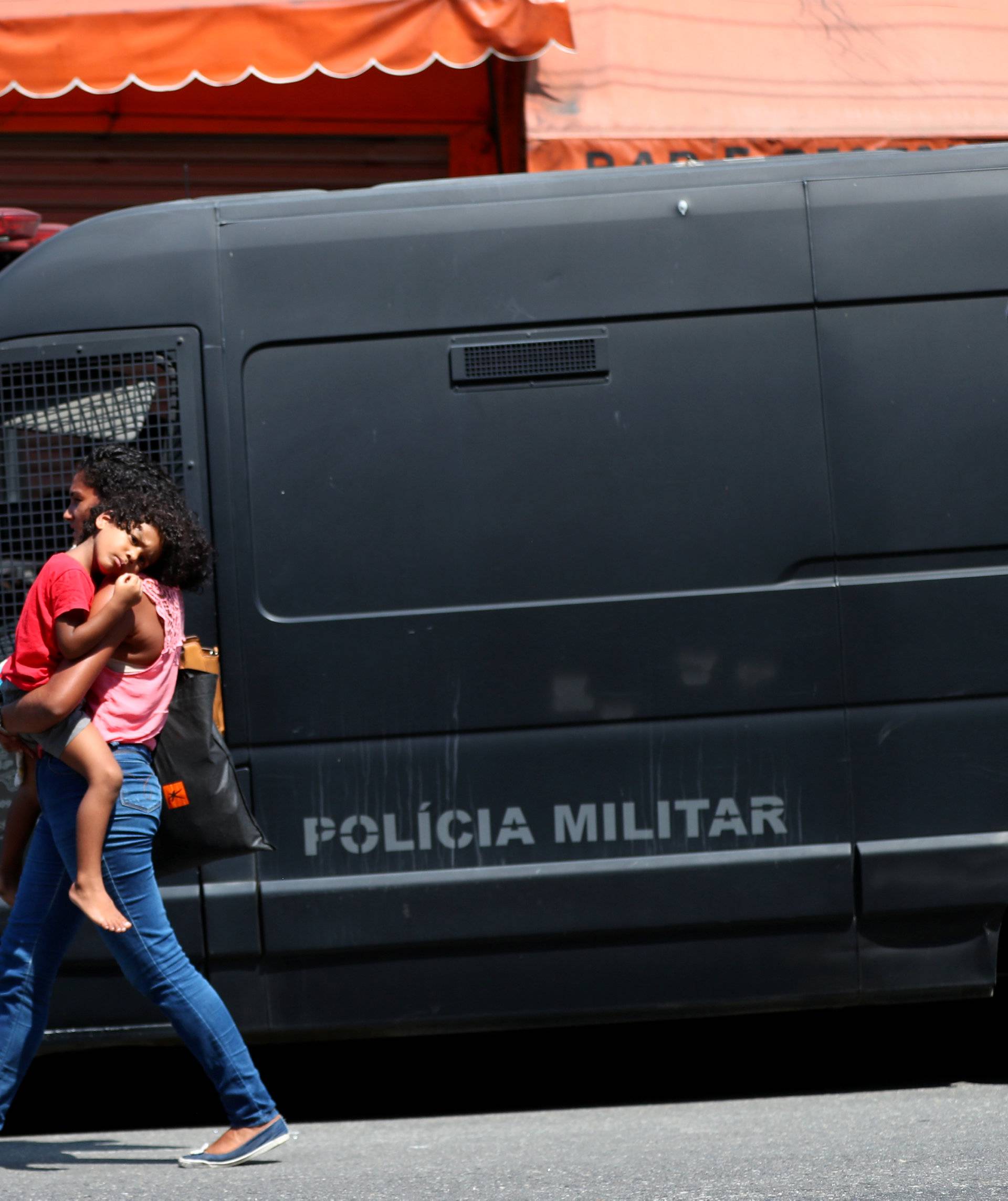 A resident walks with her child near police vehicle during an operation against drug gangs at Fallet slum in Rio de Janeiro