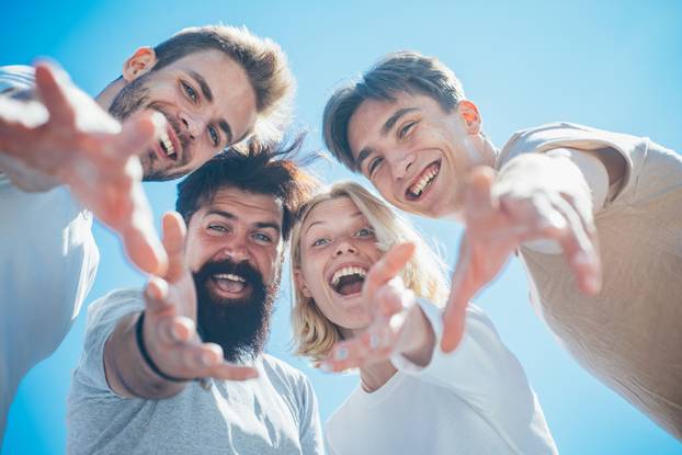 Charming blond woman with friends. Friendship huddle happiness. Trust relations and liking. Group of happy cheerful smiling friends offer their hands down to the camera at clear blue sky background.