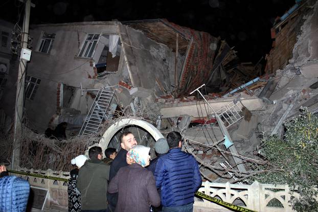 People stand outside a collapsed building after an earthquake in Elazig