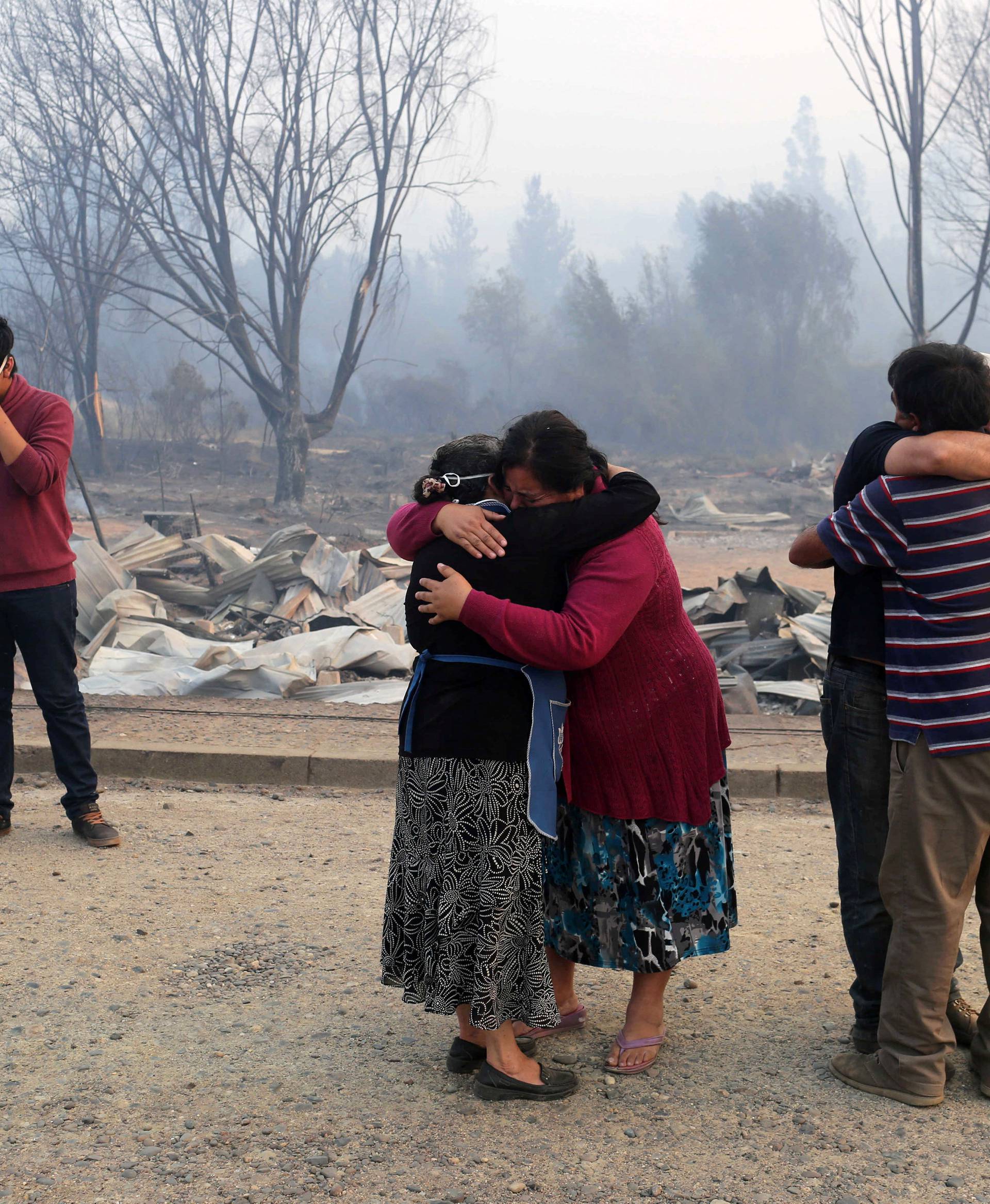 People react while standing next to burnt houses as the worst wildfires in Chile's modern history ravage wide swaths of the country's central-south regions, in Santa Olga