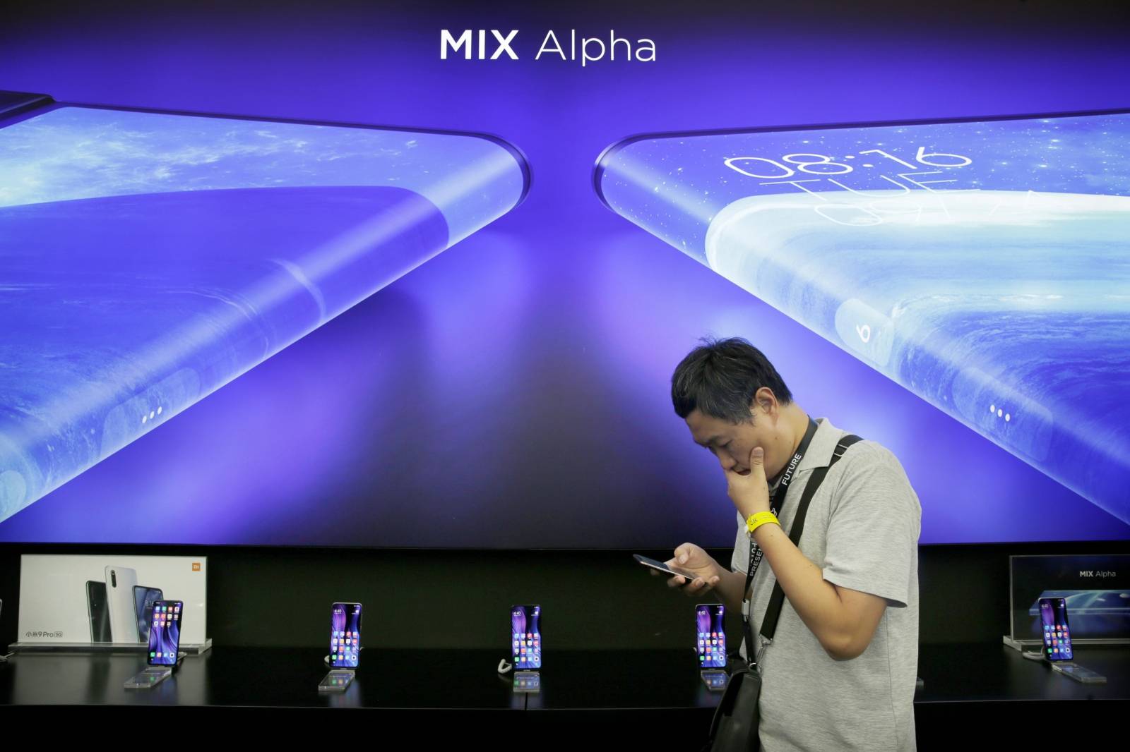 A journalist stands next to a poster of Xiaomi Mi MIX Alpha surround display 5G concept smartphone in Beijing