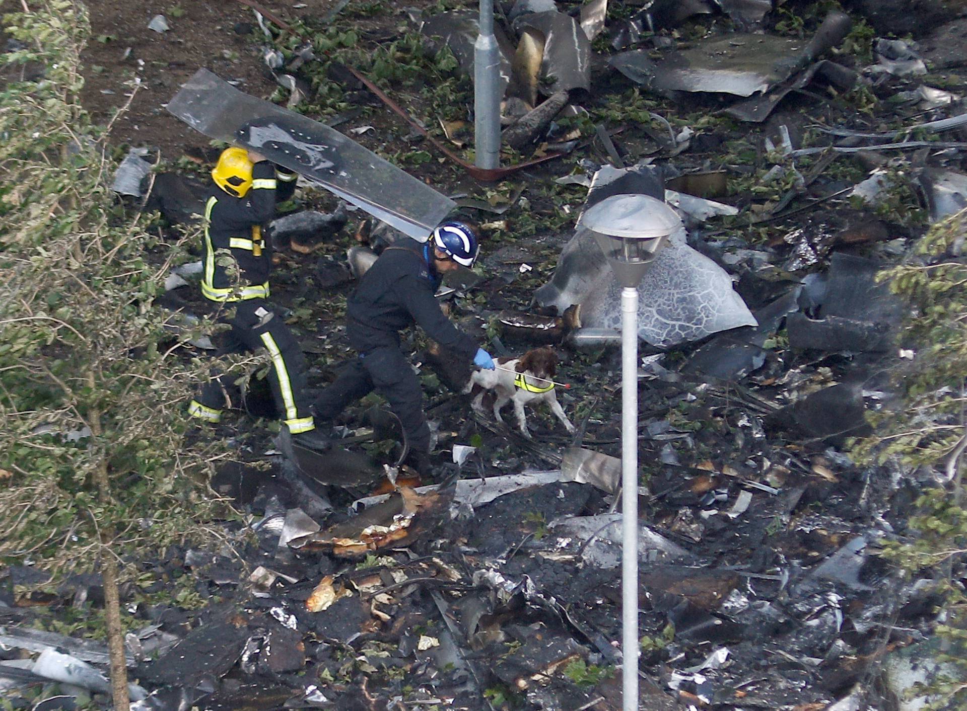 Firefighters with a dog walk around the base of the tower block that was destroyed in a fire disaster, in north Kensington, West London