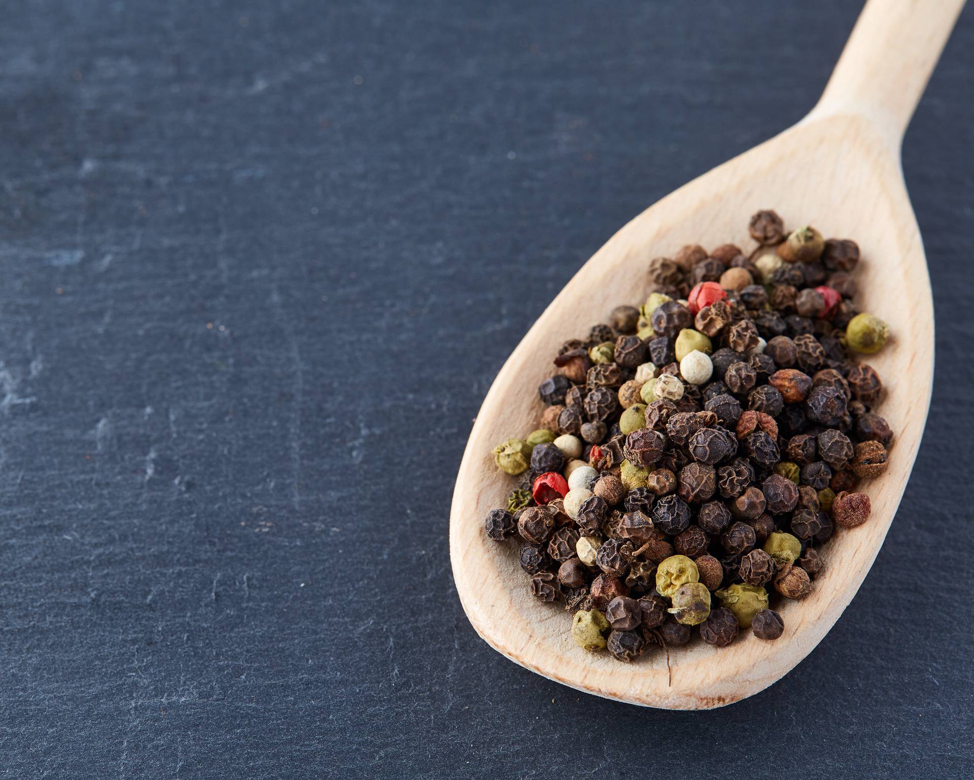 Top view of a wooden spoon full of allspice seeds isolated on dark background, shallow depth of field, front focus