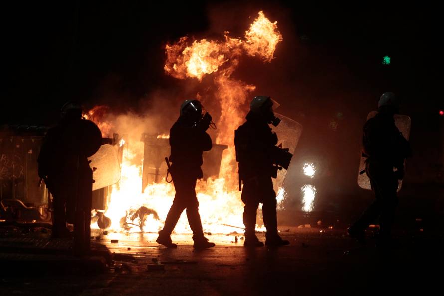 Riot police officers walk next to flames from burning garbage bins during clashes after the derby between PAOK Salonika and Olympiacos was called off in Thessaloniki