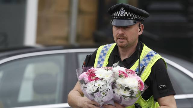 A police officer carries bunches of flowers at the scene of the murder of Labour MP Jo Cox in Birstall near Leeds