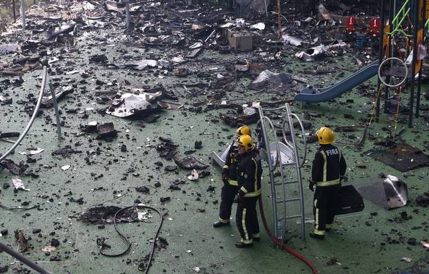 Firefighters stand amid debris in a childrens playground near a tower block severly damaged by a serious fire, in north Kensington, West London