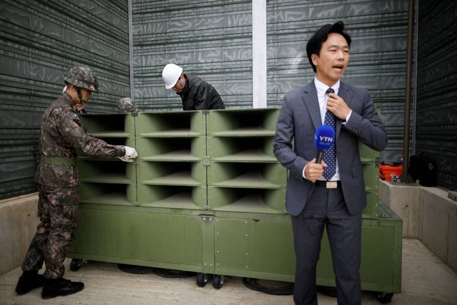 A reporter prepares a news report as South Korean soldiers dismantle loudspeakers that were set up for propaganda broadcasts near the demilitarized zone separating the two Koreas in Paju