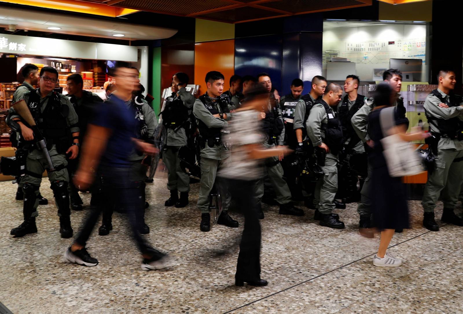 Riot police wait at a Mass Transit Railway (MTR) station as commuters walk past to catch a subway train, in Hong Kong