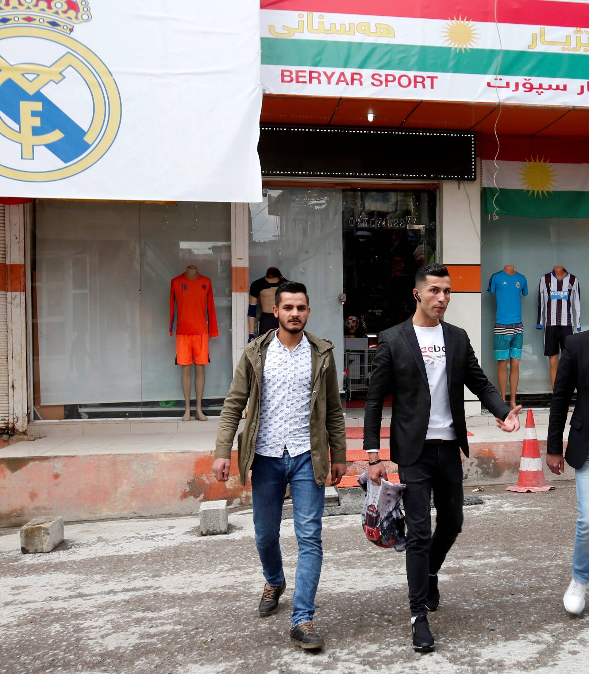 Biwar Abdullah, 25, an Iraqi Kurdish local footballer, who looks like the football player Cristiano Ronaldo, walks with his friends near a sportswear shop in the district of Soran, northeast of Erbil