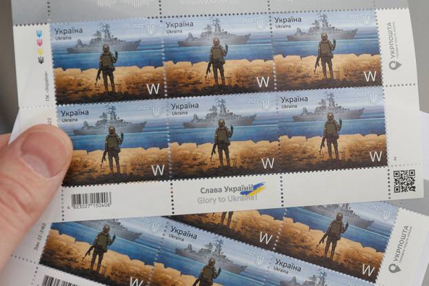 A man holds postal stamps showing Ukrainian service member and Russian warship, at the headquarters of Ukrainian post in Kyiv