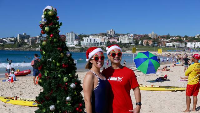 Sarah and Toby, volunteer life guards from Bondi Surf Life Saving Club, pose in front of a Christmas Tree on Bondi Beach Sydney