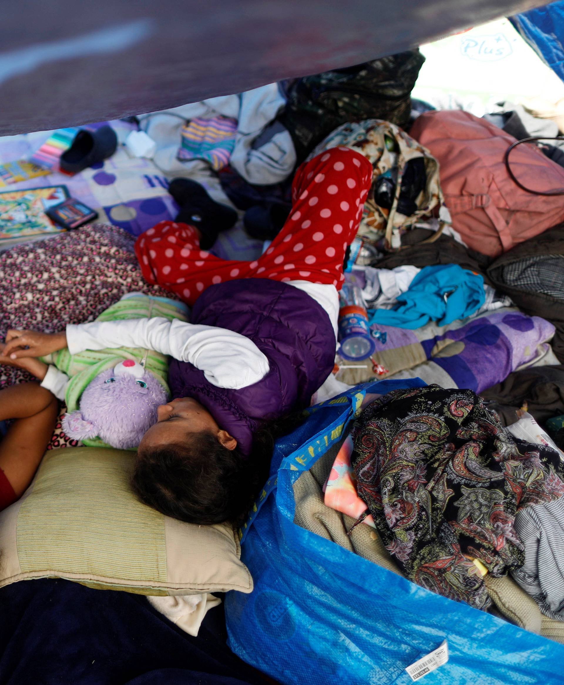 Children travelling with a caravan of migrants from Central America rest under a plastic tarp at a camp near the San Ysidro checkpoint, in Tijuana