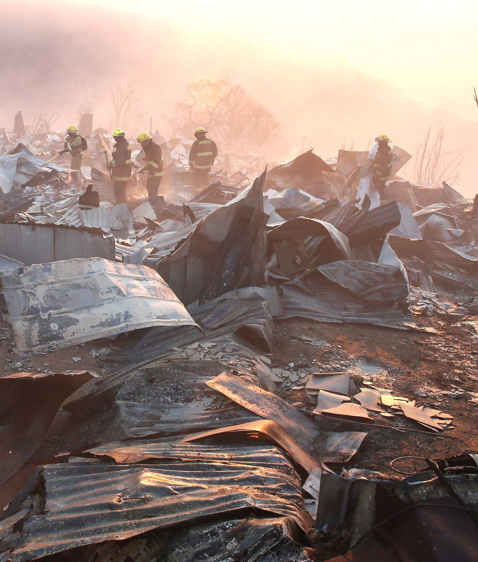 Firefighters remove the remains of a burned house on a hill, where more than 100 homes were burned due to forest fire but there have been no reports of death, local authorities said in Valparaiso, Chile