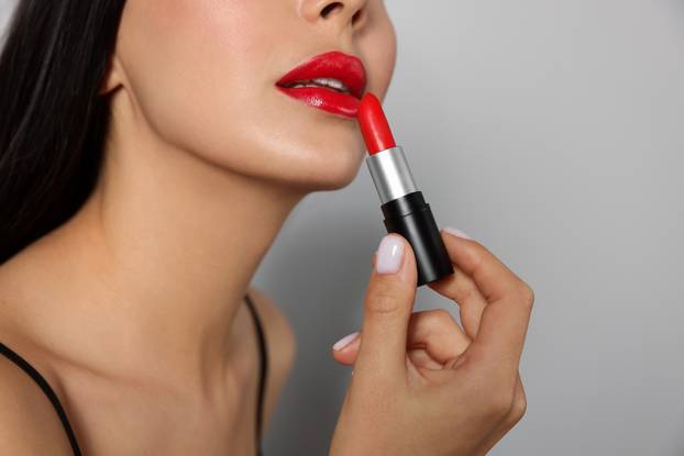 Young woman applying red lipstick on light gray background, clos