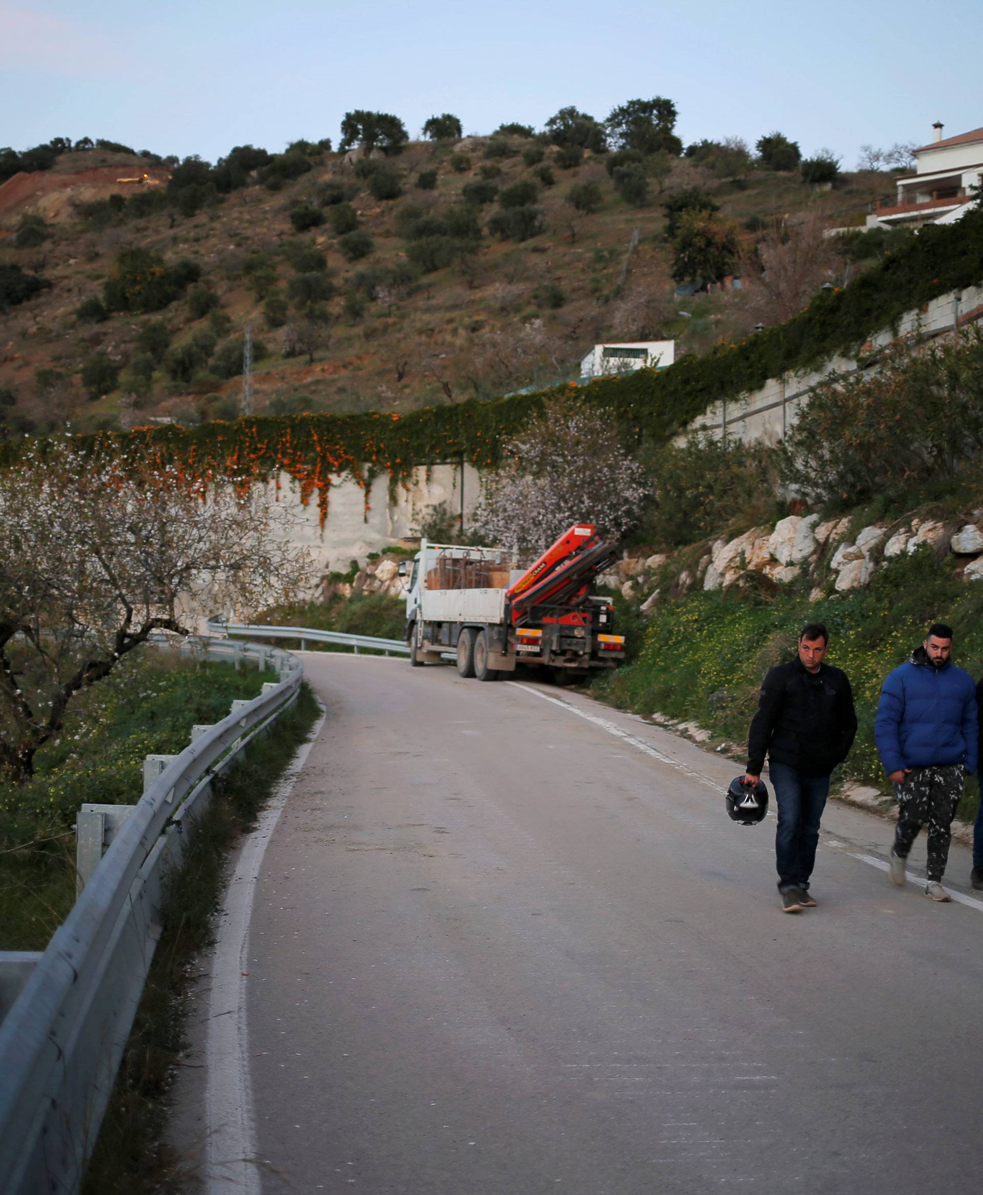 People walk along a road after leaving the area (top) where Julen, a Spanish two-year-old boy fell into a deep well four days ago when the family was taking a stroll through a private estate, in Totalan