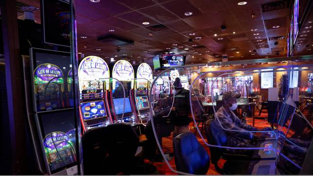 People sit wearing protective face masks, amid the coronavirus disease (COVID-19) pandemic, behind plastic barriers playing slot machines at the Ute Mountain Hotel and Casino in Towaoc, Colorado