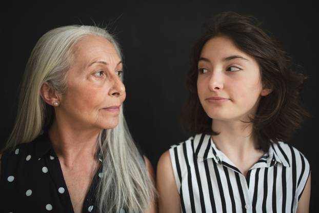 Portrait of senior grandmother with her granddaughter looking at each other over black blackground
