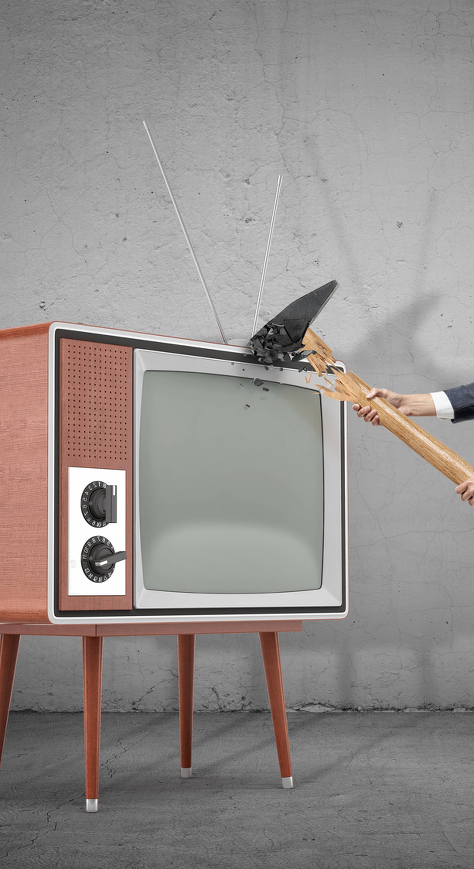 A businessman on concrete background fails to smash an old retro TV set with a broken hammer.