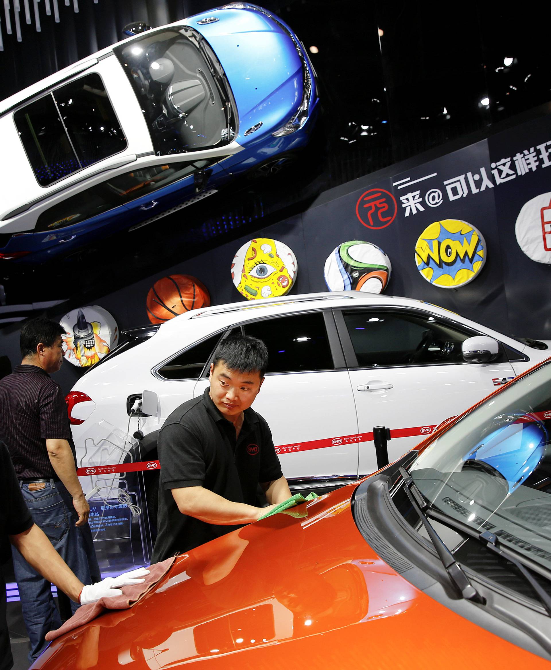 Members of staff clean a vehicle presented at BYD booth during Auto China 2016 auto show in Beijing