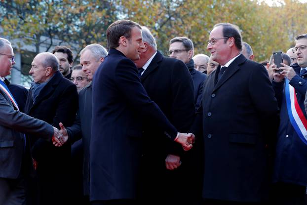 French President Emmanuel Macron shakes hands with former French President Francois Hollande as they stand in front of a commemorative plaque outside the Stade de France stadium, in Saint-Denis, near Paris
