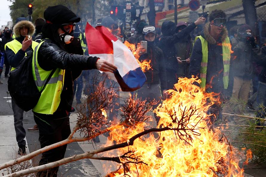A protester wearing a yellow vest burns a French flag at a barricade during clashes with police as part of a national day of protest by the "yellow vests" movement in Paris