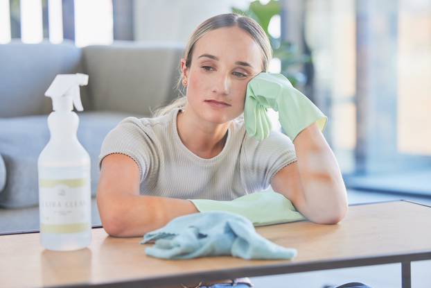 Woman, tired and burnout after cleaning house, office or home with spray, chemical or sanitizer. Cleaner, gloves and table for domestic work, job or service take time to rest, breathe and relax