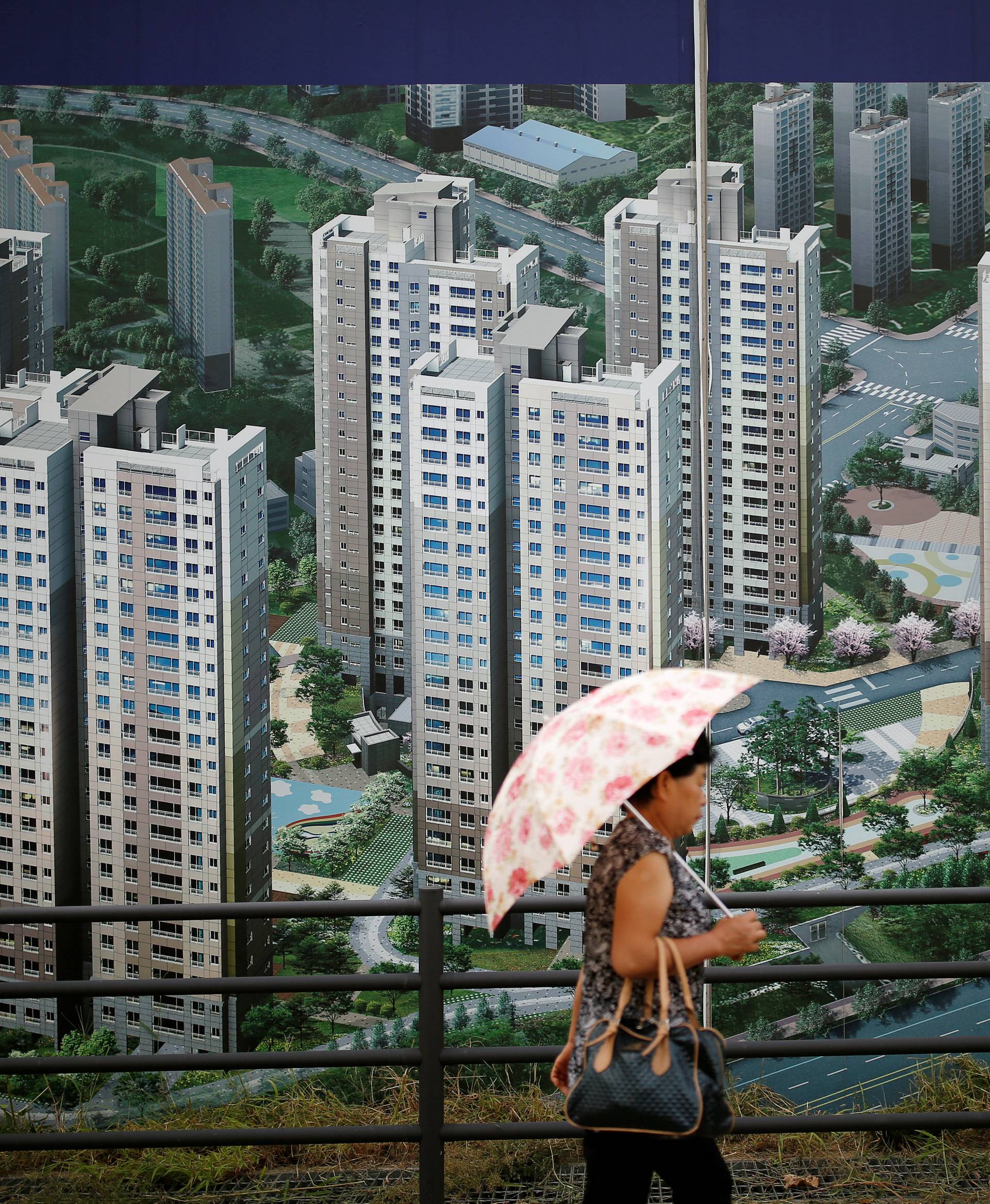 A woman walks past an advertisement promoting an apartment complex which is currently under construction in Yongin