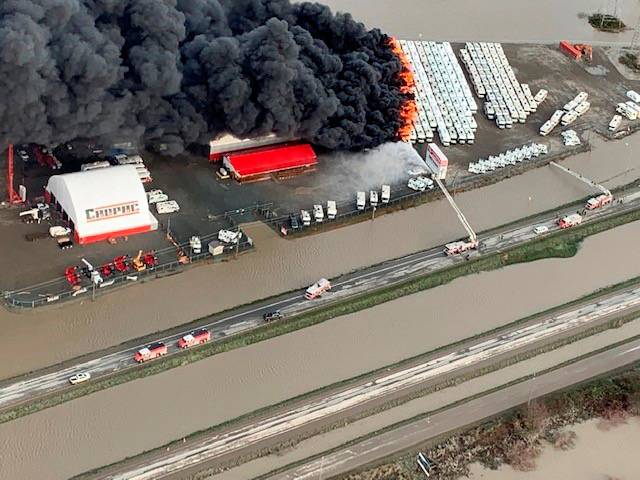 Vehicle holding lot on fire surrounded by flood waters in Abbotsford, British Columbia
