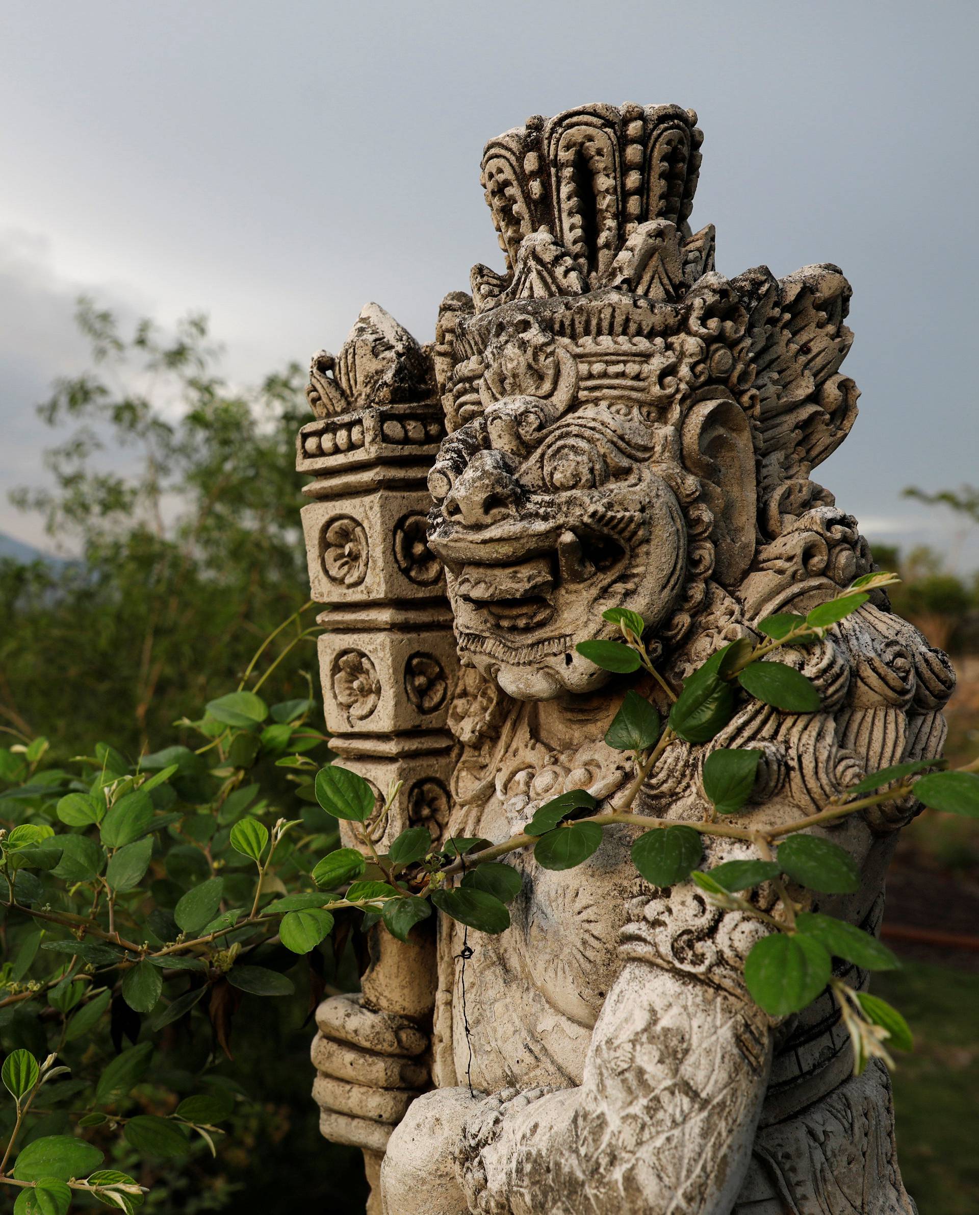 A statue on a bridge is seen as Mount Agung volcano erupts in the background near Kubu in Bali