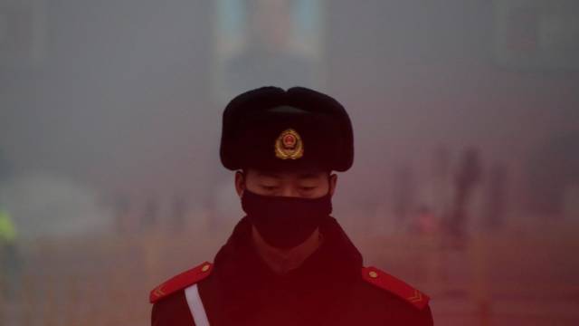 FILE PHOTO: A paramilitary police officer wearing a mask stands guard in front of a portrait of the late Chairman Mao during smog at Tiananmen Square in Beijing