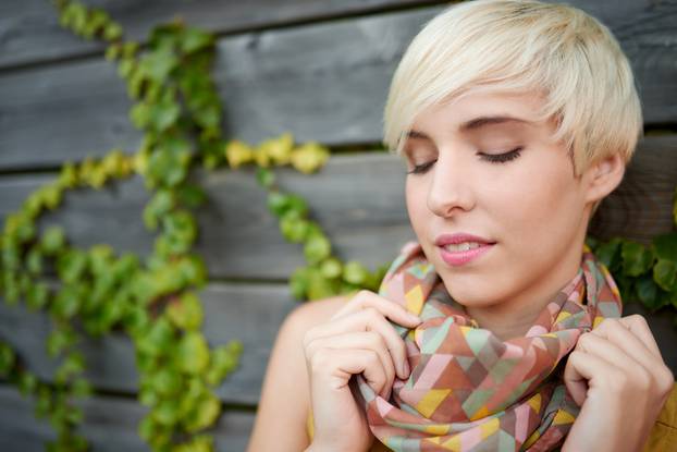 Beautiful short haired platinum blond woman standing against an ivy fence backdrop