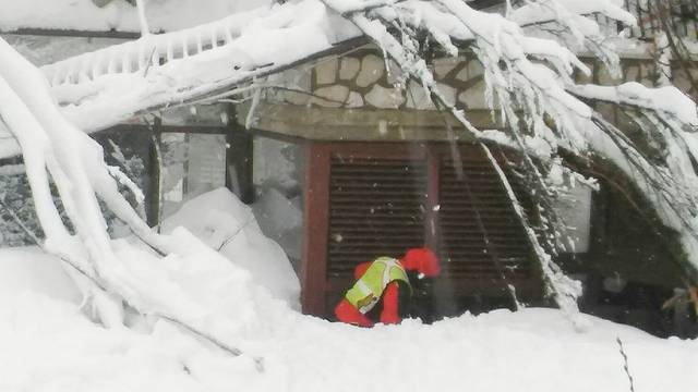 A member of Lazio's Alpine and Speleological Rescue Team is seen in front of the Hotel Rigopiano in Farindola