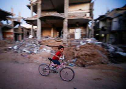 A boy rides his bicycle near the rubble of a house which was destroyed by Israeli air strikes during the Israel-Hamas fighting, in Gaza Strip