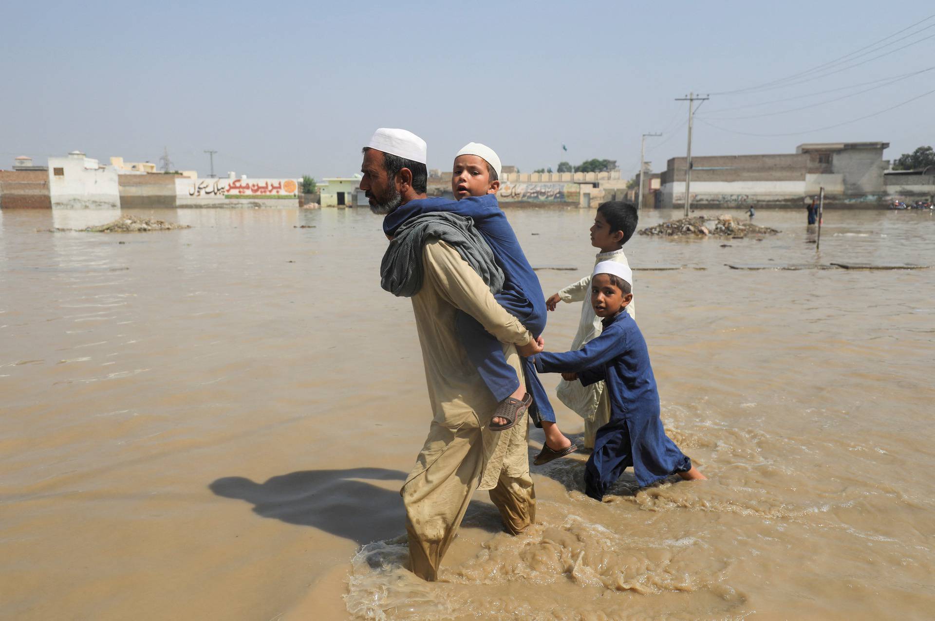 A man walks with children amid flood water along a road, following rains and floods during the monsoon season in Nowshera
