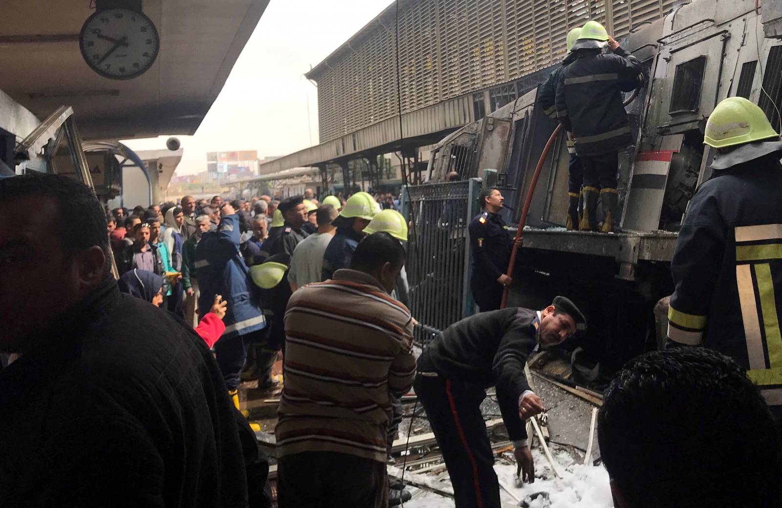 Member of security forces gestures as rescue workers and people gather at the scene after a fire caused deaths and injuries at the main train station in Cairo