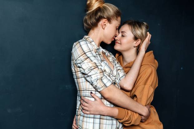 Loving lesbian girls hugging, standing on background of blue wall. Same sex love, gay marriage, lesbian couple Concept