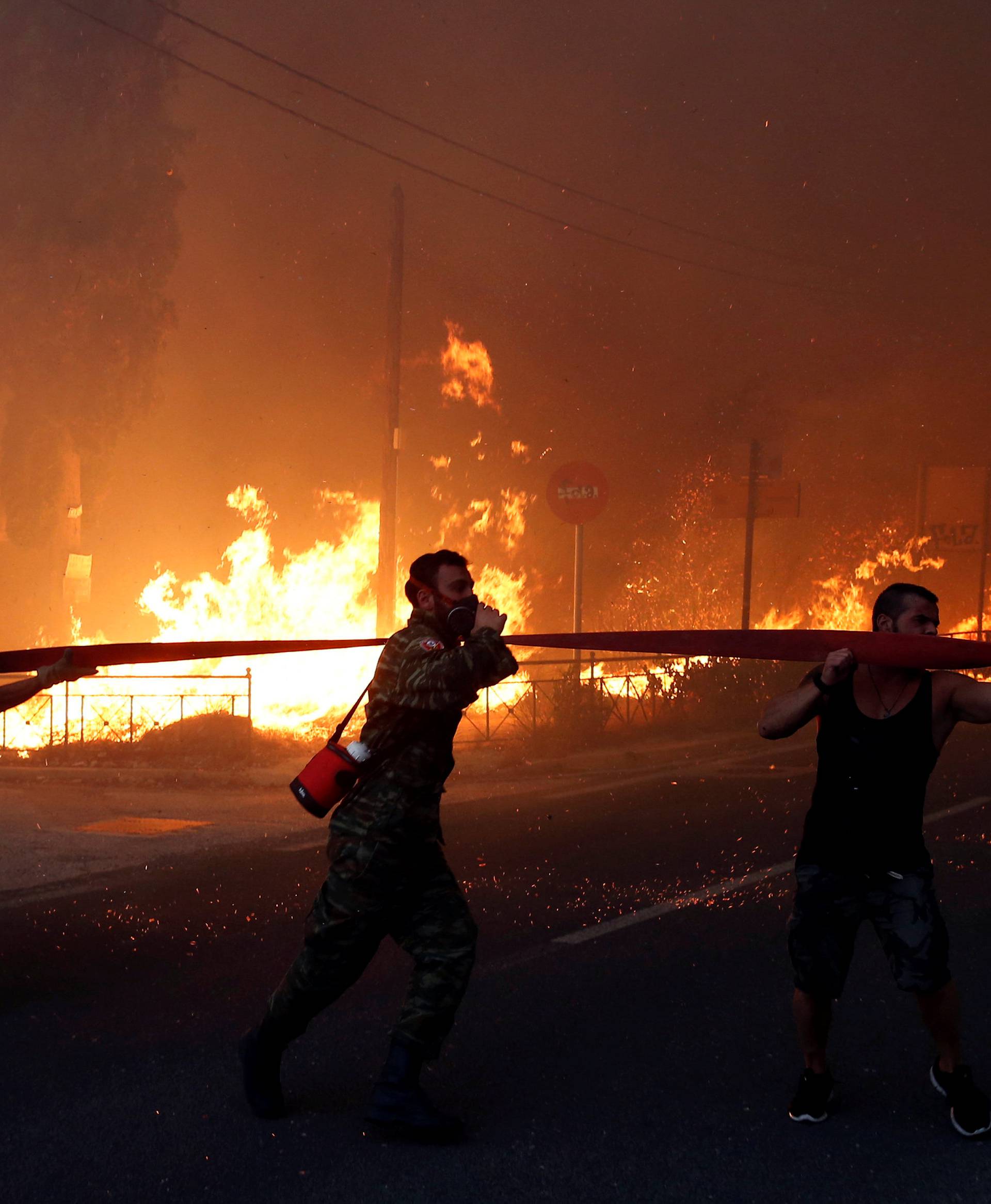 Firefighters, soldiers and local residents carry a hose as a wildfire burns in the town of Rafina, near Athens