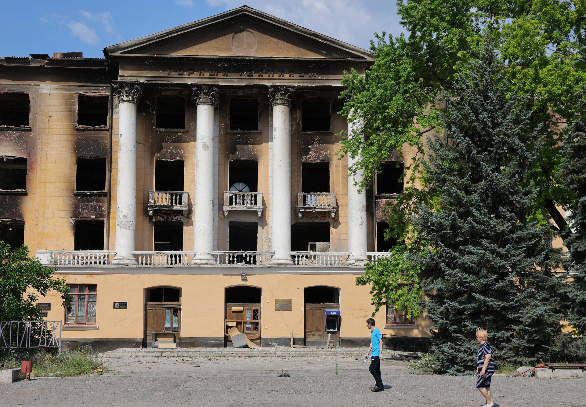 Local residents walk near a damaged building of the Lysychansk State Mining and Industrial College in Lysychansk