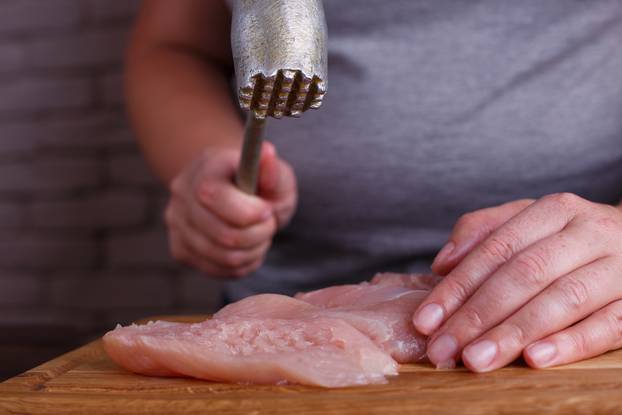 Overweight woman hands beating chicken breasts with meat hammer,