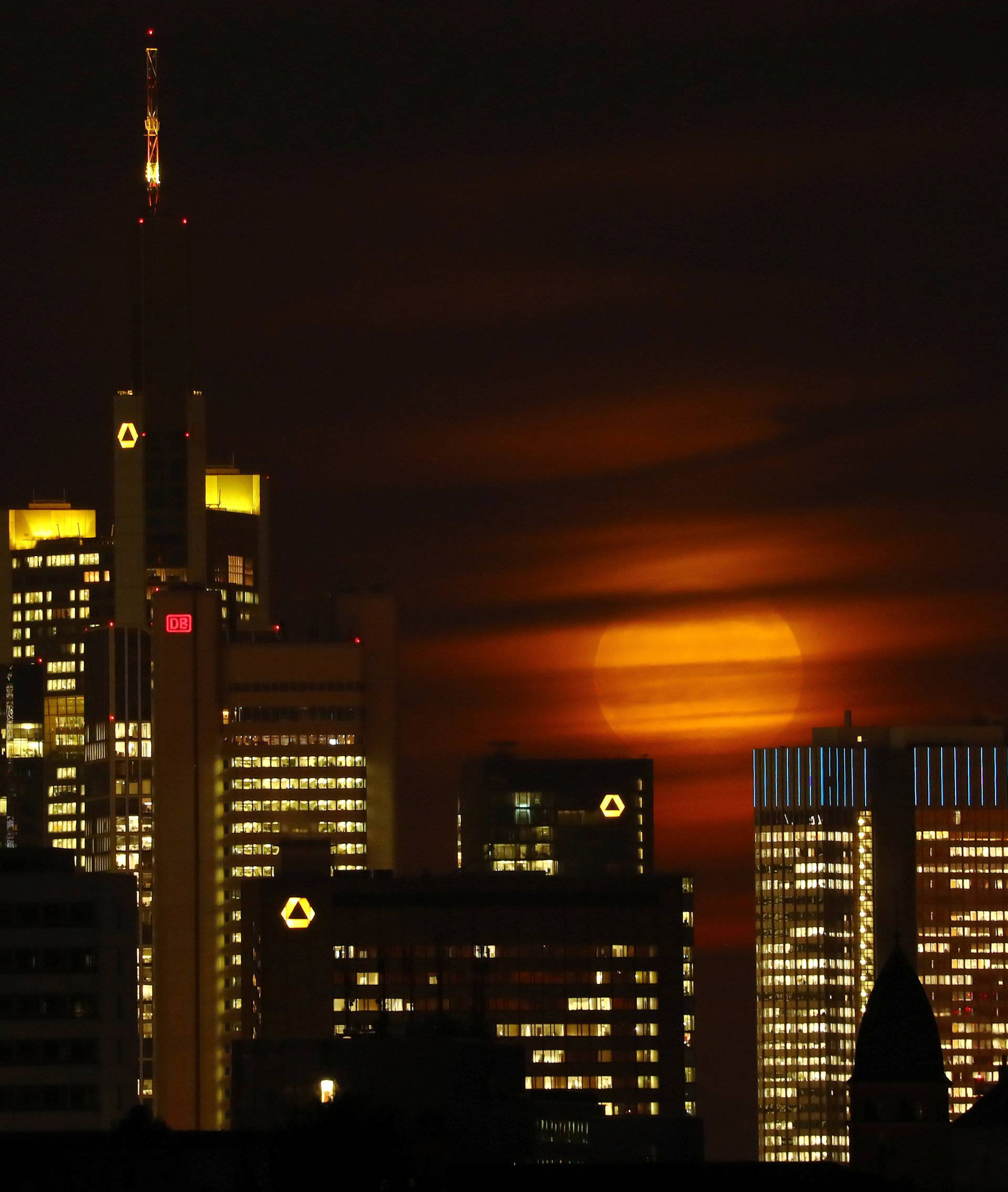 The moon is partly covered by clouds as it rises above the skyline of Frankfurt 