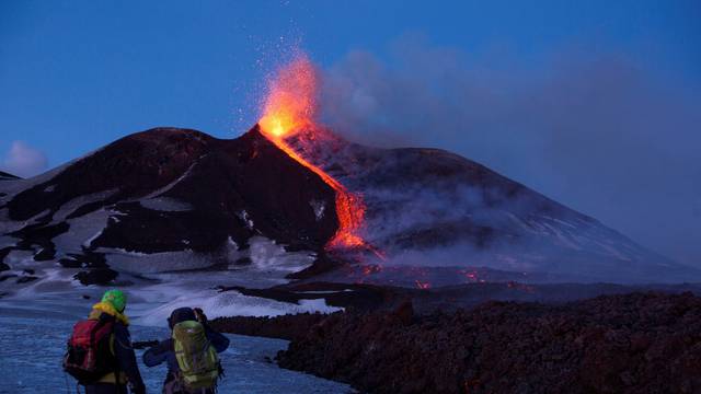 FILE PHOTO: Volcano guides stand in front of Italy's Mount Etna, Europe's tallest and most active volcano, as it spews lava during an eruption on the southern island of Sicily