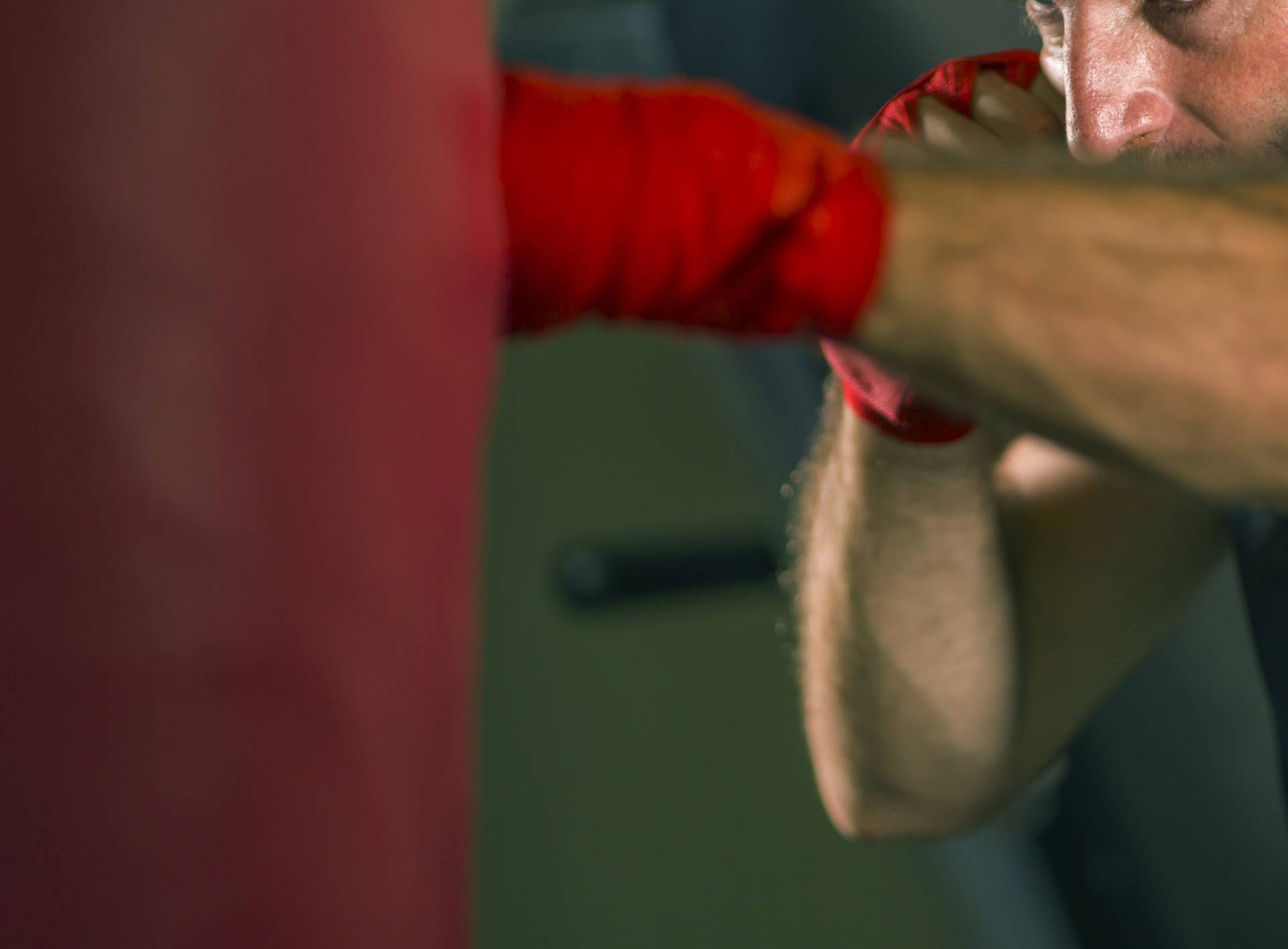 lifestyle gym portrait of young attractive and fierce looking man training boxing at fitness club doing heavy bag punching workout with wrist wraps in badass fighter look 