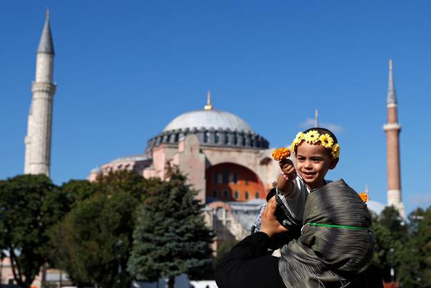 Woman holds a child in front of Hagia Sophia or Ayasofya-i Kebir Camii in Istanbul